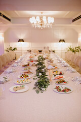 Restaurant, banquet, table setting. The table is covered with a white tablecloth, dishes, white clean plates, cutlery, napkins, wine glasses, candles. Close-up.