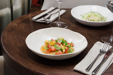 Healthy eating concept. Fresh fruit salad with strawberry, passion fruit, kiwi, peach, leaf, and micro greens with a glass of clean water on a table in a restaurant.