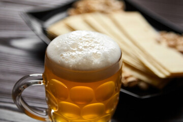 Mug of unfiltered light wheat beer with beer snacks on wooden table