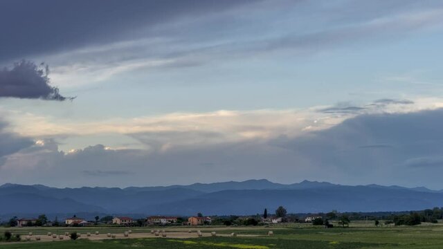 Beautiful and colorful sunset over the fields with hay bales to dry and in the background the mountains that separate Tuscany from Emilia Romagna, central Italy. Time lapse motion