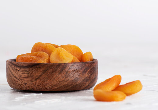 Closeup of a wooden bowl with dried apricots on a white background.