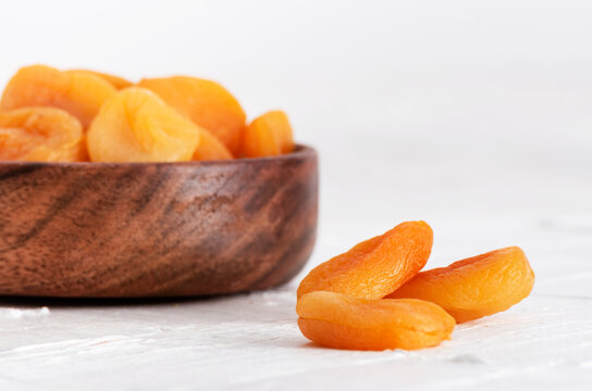 Closeup of a wooden bowl with dried apricots on a white background.