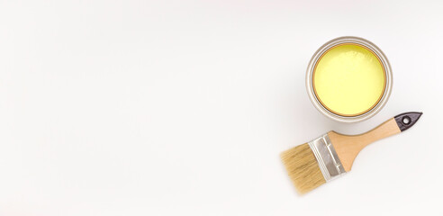 A paintbrush and a can of yellow paint on the side on a light background. Top view, banner. Renovation concept.