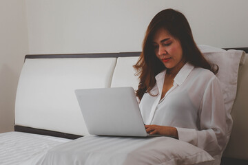 Relaxing work at home, concept with a women sitting on the bed with laptop and other tools.