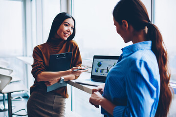 Two adult female colleagues discussing work ideas in office interior