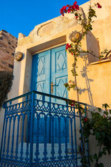 blue door in the wall of a typical house in santorini with pink flower plant