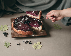 Round blueberry pie sprinkled with powdered sugar cut on a wooden board on the table on a gray background. A piece is taken with a spoon.	