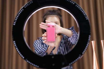 Woman vlogger holding perfume in hands, looking in camera while recording video for blog.