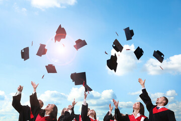 Happy students throwing graduation hats in air outdoors