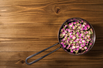 Small tea rose buds in a stewpan, top view. Wood background.