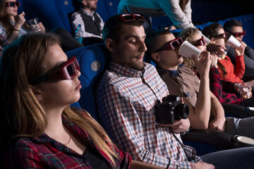 a young guy, looking around, in fear of being seen behind an illegal pirate video in a movie theater. Against the backdrop of sitting people of different sexes watching a movie in the cinema