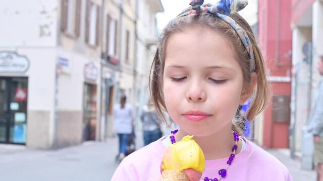 Little girl eats italian ice cream on the street of the old city. Bright milk-free popsicles in the hands of a 7-year-old child. The concept of relaxation and good food for children and adults.