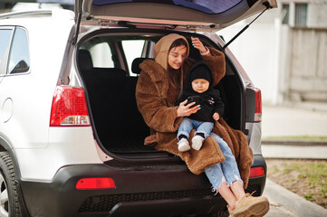Young mother and child sitting in the trunk of a car and looking at mobile phone. Safety driving concept.