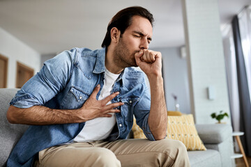 Fototapeta premium Young man feeling ill and coughing at home.