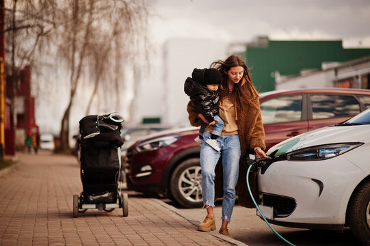 Young Mother With Child Charging Electro Car At The Electric Gas Station.