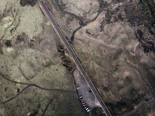 The road is surrounded by volcanic lava, aerial view from top to bottom. Parked cars. Tianfaya...