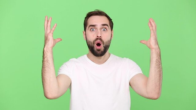 Bearded fun young guy 20s in white t-shirt isolated on green chroma key background studio. People sincere emotions lifestyle concept. Looking shocked surprised wow showing hands brain explosion head