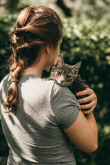 Young white woman holds in hands small beautiful striped gray kitten outdoors in summer park. © lesia17