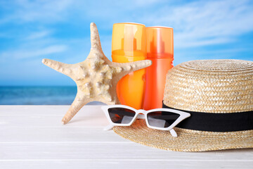 Set of sun protection products and stylish accessories on white wooden table near sea