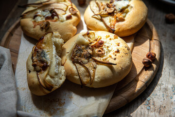 Homemade hand pizzas with pear, ricotta, gorgonzola and hazelnuts on round wooden board.