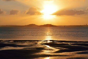 Fototapeta na wymiar Sunset over sandy beach. Wet sand reflects sunlight
