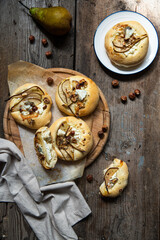 Homemade hand pizzas with pear, ricotta, gorgonzola and hazelnuts on round wooden board.
