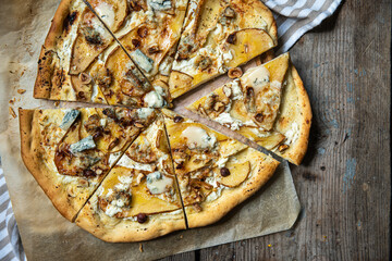 Sliced homemade pizza with pear, gorgonzola, ricotta and hazelnuts on baking paper on wooden background..