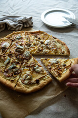 Woman hand holding slice of homemade pizza with pear, gorgonzola, ricotta and hazelnuts on baking paper.