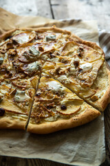 Sliced homemade pizza with pear, gorgonzola, ricotta and hazelnuts on baking paper.