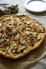 Sliced homemade pizza with pear, gorgonzola, ricotta and hazelnuts on baking paper.