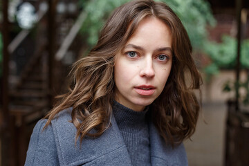 Fototapeta premium closeup on young thoughtful pretty girl in gray coat and turtleneck posing outdoors. Street style portrait photo session of attractive female, urban photoshoot of beautiful elegant model, close up