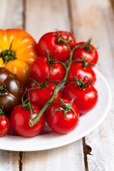 Ripe colorful yellow and red tomatoes on white plate, wooden background. Variety of shapes, colors. Healthy light summer meal, delicious low calories vegetable. Close up