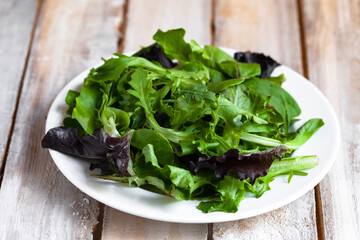Concept of healthy food, clean eating, low calories meal, organic products. White plate with green salad on wooden background. Spinach, aragula, letucce. Close up