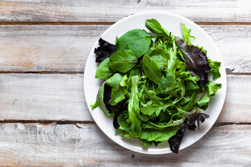 Concept of healthy food, clean eating, low calories meal, organic products. White plate with green salad on wooden background. Spinach, aragula, letucce. Top view flat lay copy space for text
