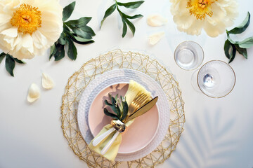 Contemporary table setting with peony flowers and golden utensils on white table. Modern trendy...