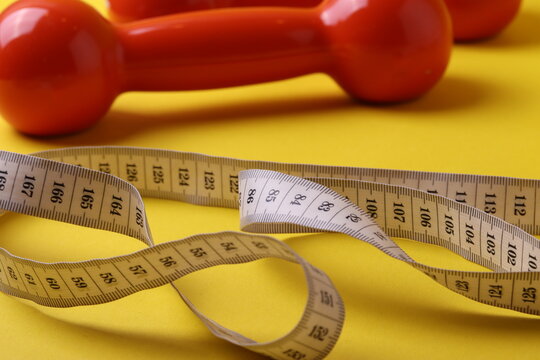 Orange Small Dumb Bells On The Yellow Background, Representing Healthy Lifestyle Or Sport Motivation Concept