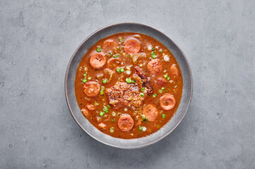 Chicken and Sausage Gumbo soup in gray bowl on concrete backdrop. Gumbo is louisiana cajun cuisine soup with roux. American USA Food. Traditional ethnic meal
