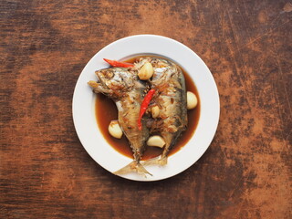 Top view Thai mackerel in dark soy sauce with garlic and red chili pepper on wooden table