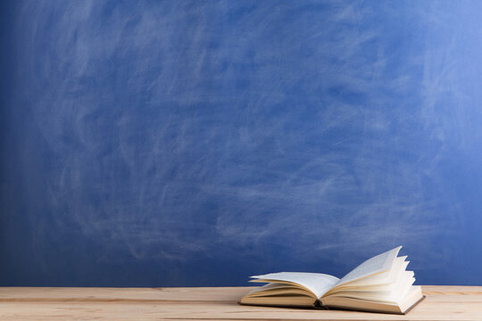 Education and reading concept - group of books on the wooden table, blue blackboard background. Teachers desk