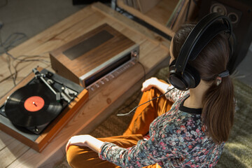 Young Woman listening a music on a HiFi system with turntable, amplifier, headphones and lp vinyl...