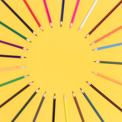 Circle frame made of colorful pencils on a yellow background. Artistic template with place for text.