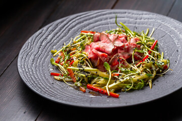 Authentic salad with bacon fresh red pepper, sprouts, sesame and olive oil on a black plate. Morning atmospheric lighting, fashionable trendy spot soft focus. Preparation for design creative menu.