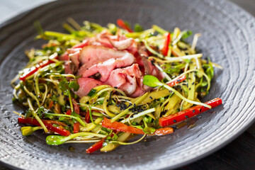 Authentic salad with bacon fresh red pepper, sprouts, sesame and olive oil on a black plate. Morning atmospheric lighting, fashionable trendy spot soft focus. Preparation for design creative menu.