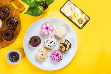 Colourful doughnuts served on a white plate on yellow background.
