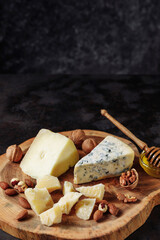 Cheese platter with honey and various nuts on an authentic wooden board. Dark black embossed background. Appetizer, aperitif, snack table