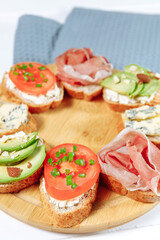 Tomato bruschette snack on a wooden plate on a white wooden table and gray napkin. Mini sandwich mix