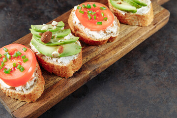 Assorted vegan bruschette snack on a wooden chopping board on a dark textured table. Mini sandwich mix. Top view, close up