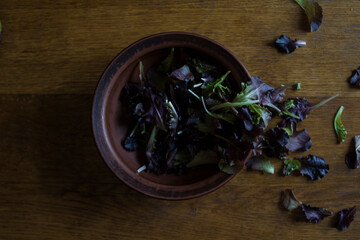 Colored salad lies in a natural clay pot on a wooden oak table