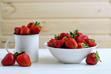Red ripe strawberries in a white plate on a white wooden table. Fresh berries, healthy food, detox for the body, vegetarian.