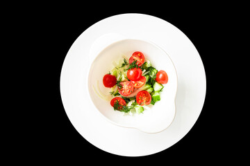 Fresh summer salad of cherry tomatoes and cucumber with herbs on a white plate on a black background